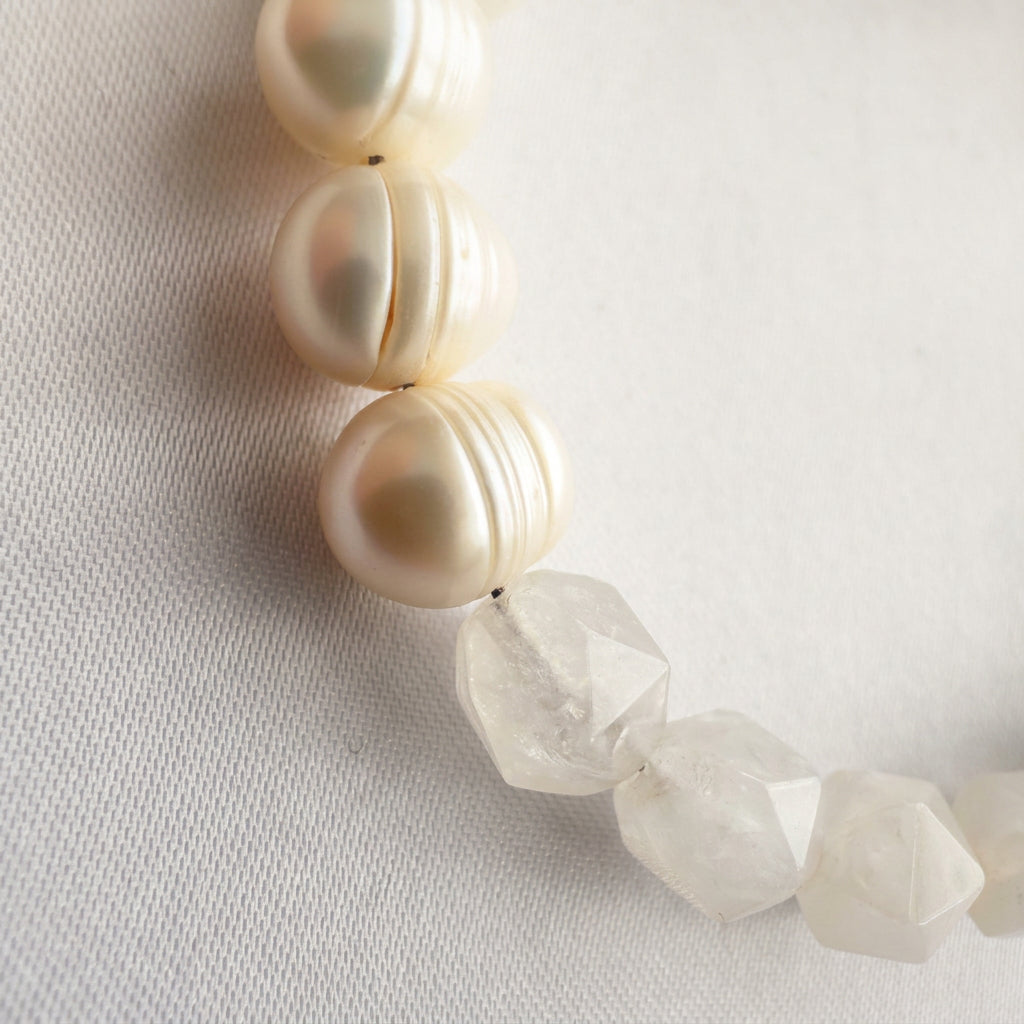 Close-up of faceted clear quartz beads meeting creamy white baroque pearls on pale linen, highlighting the quartz’s angular surfaces and the pearls’ natural ridges.