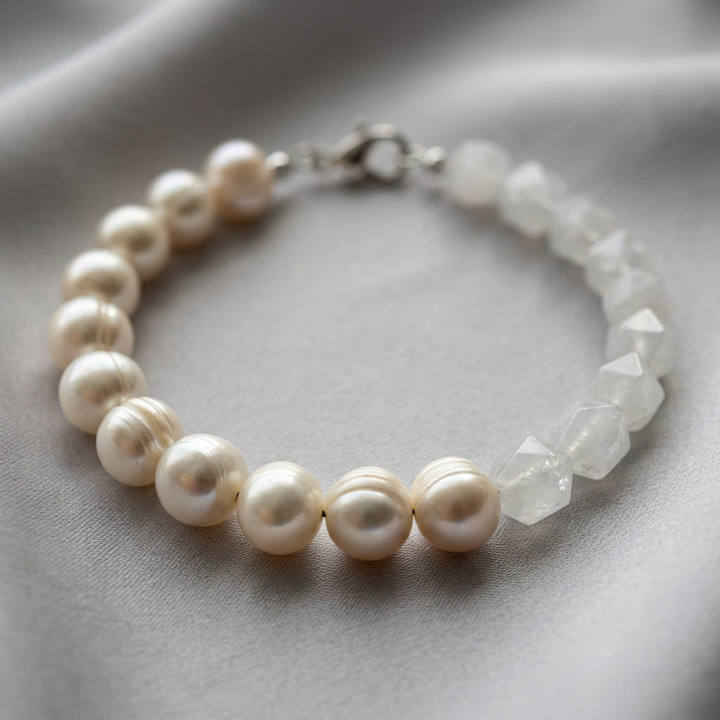 Bracelet arranged in an oval on grey fabric, with creamy white ribbed baroque pearls along one side, faceted clear quartz beads along the other and a sterling silver lobster clasp.