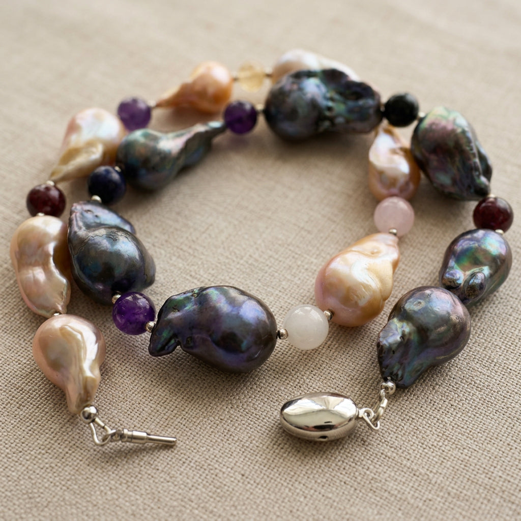 Dark blue-grey and golden-cream keshi pearl necklace coiled on linen with multicoloured gemstone beads and an unfastened sterling silver clasp, showing the separate clasp body and insert.