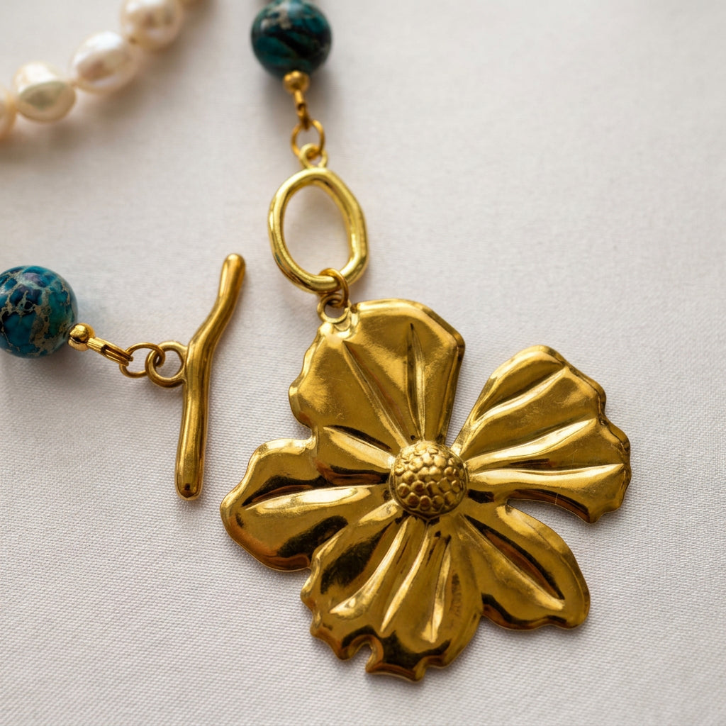 Close-up of loosely coiled necklace strands with mottled blue jasper beads, pairs of creamy white baroque pearls and gold-coloured hematite spacers on cream fabric.