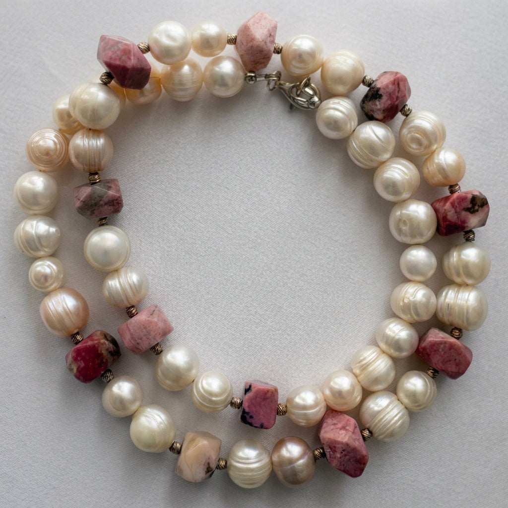 White baroque pearl and pink opal necklace loosely coiled on pale fabric, showing large ridged pearls, irregular pink stones with dark mottling, textured sterling silver spacers and a clasp near the top.