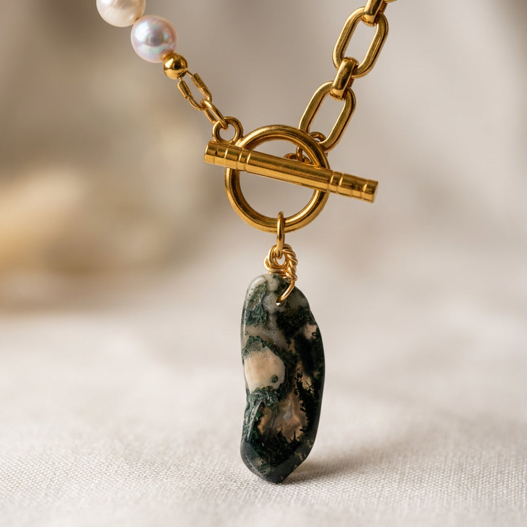 Close-up of an elongated green Indian agate pendant with cream inclusions and gold-coloured wire wrapping, hanging beneath a fastened gold-plated toggle clasp between white pearls and paperclip chain.⠋