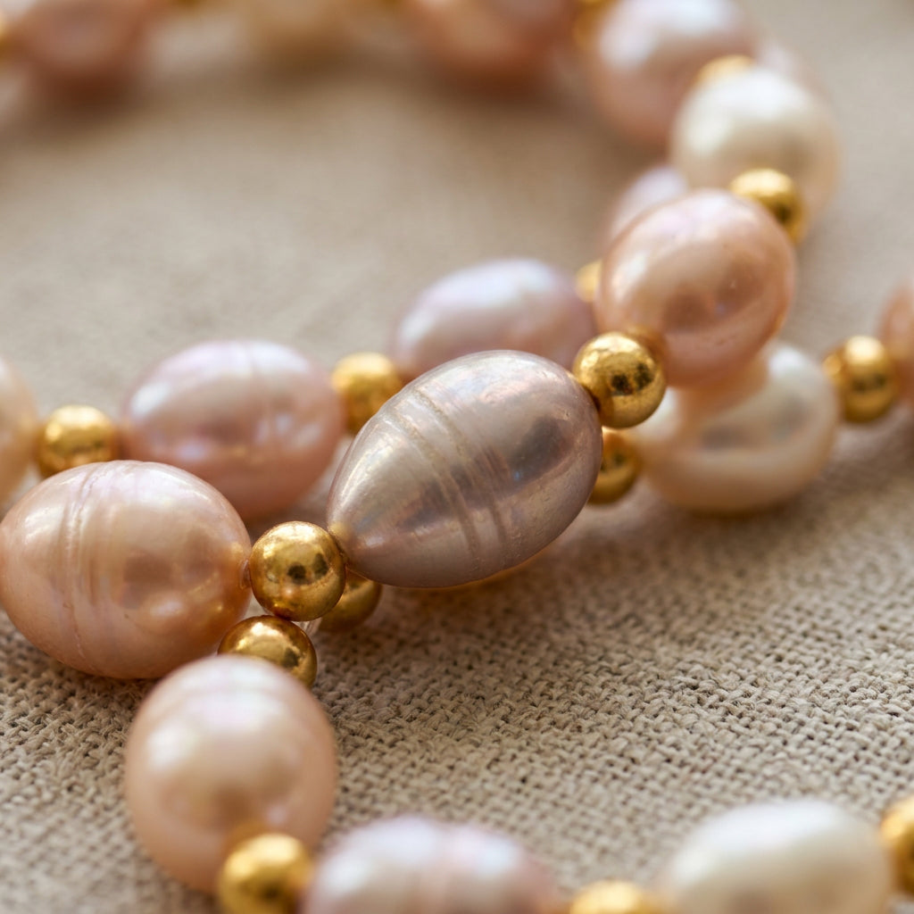 Close-up of blush pink, lilac and creamy white baroque pearls with gold-plated spacer beads on linen, highlighting their natural surface ridges and iridescent lustre.⠋