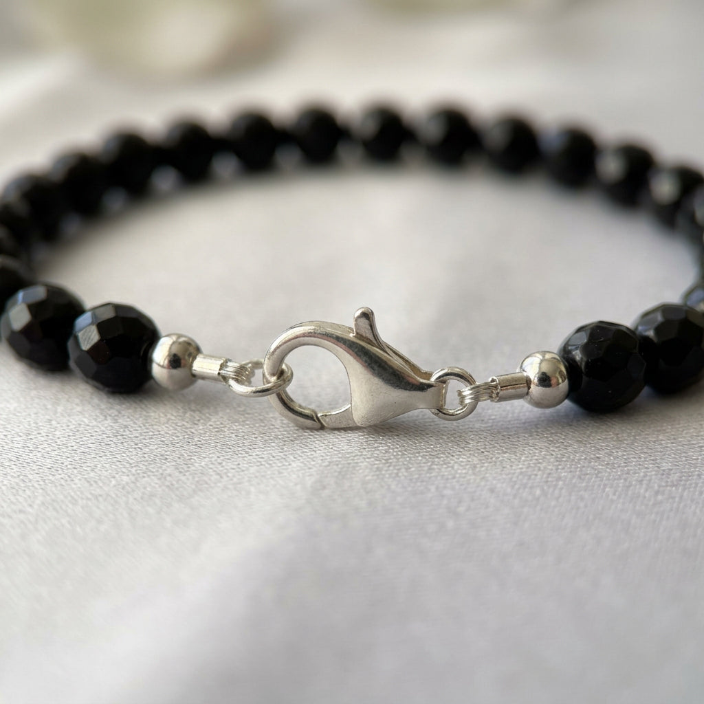 Close-up of a fastened sterling silver lobster clasp and polished end beads on a faceted black onyx necklace, resting on cream fabric.
