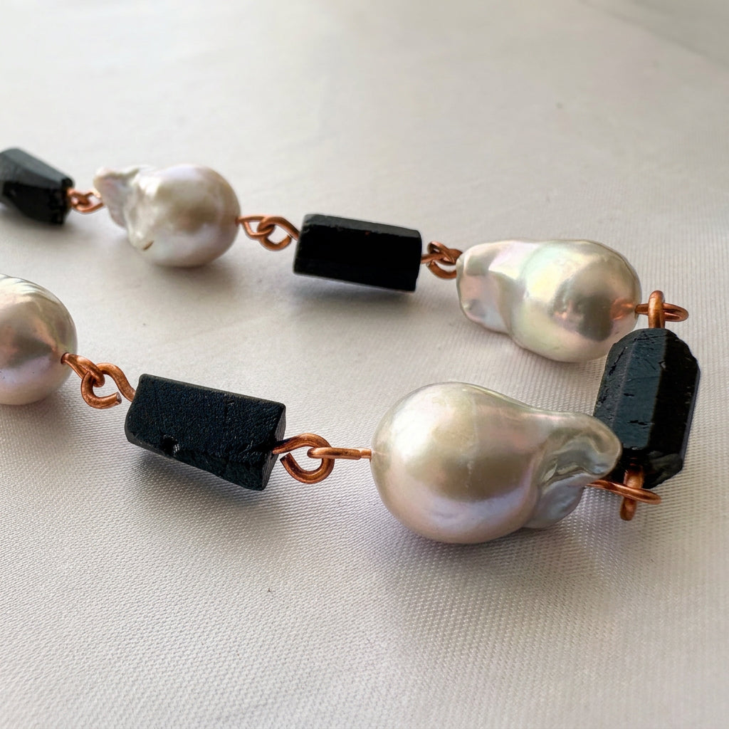 Handmade copper S-hook clasp fastened through circular connecting rings, with copper chain extending to either side on pale fabric.