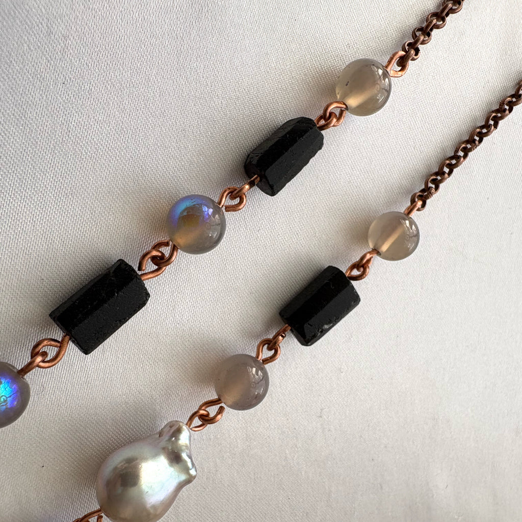 Copper wire necklace laid on pale fabric, showing raw black tourmaline crystals, grey labradorite beads with blue flashes, a silver Keshi pearl and copper chain.