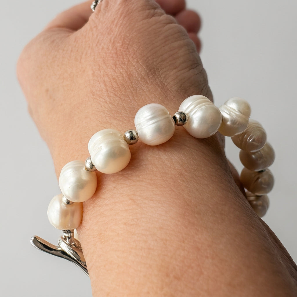 White baroque pearl bracelet worn on a wrist, showing rounded, irregular pearls with natural ridges and soft lustre, separated by small silver-coloured beads.