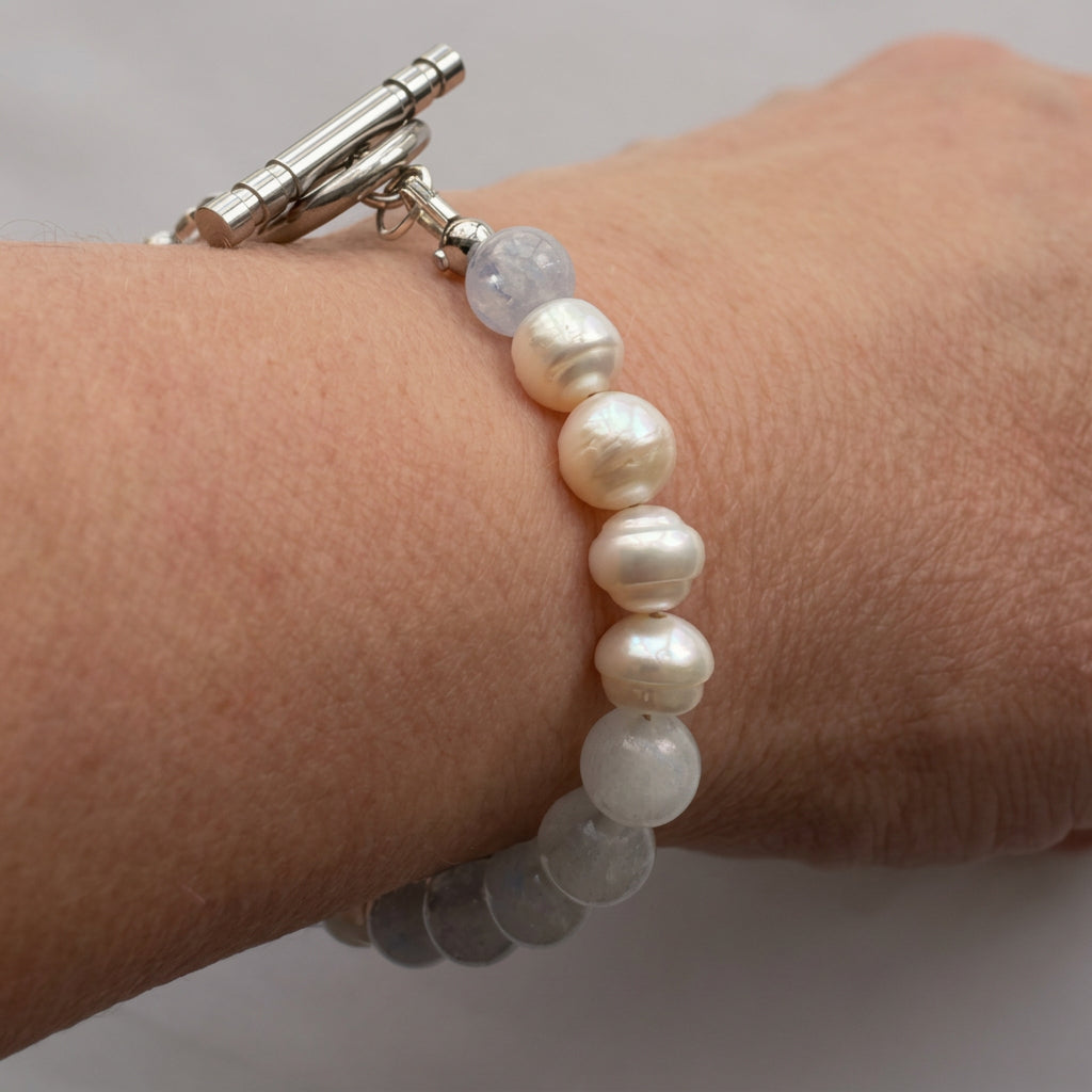 Side view of a white baroque pearl and aquamarine bracelet worn on a wrist, showing naturally ridged pearls, pale blue beads and a stainless steel toggle clasp.⠋