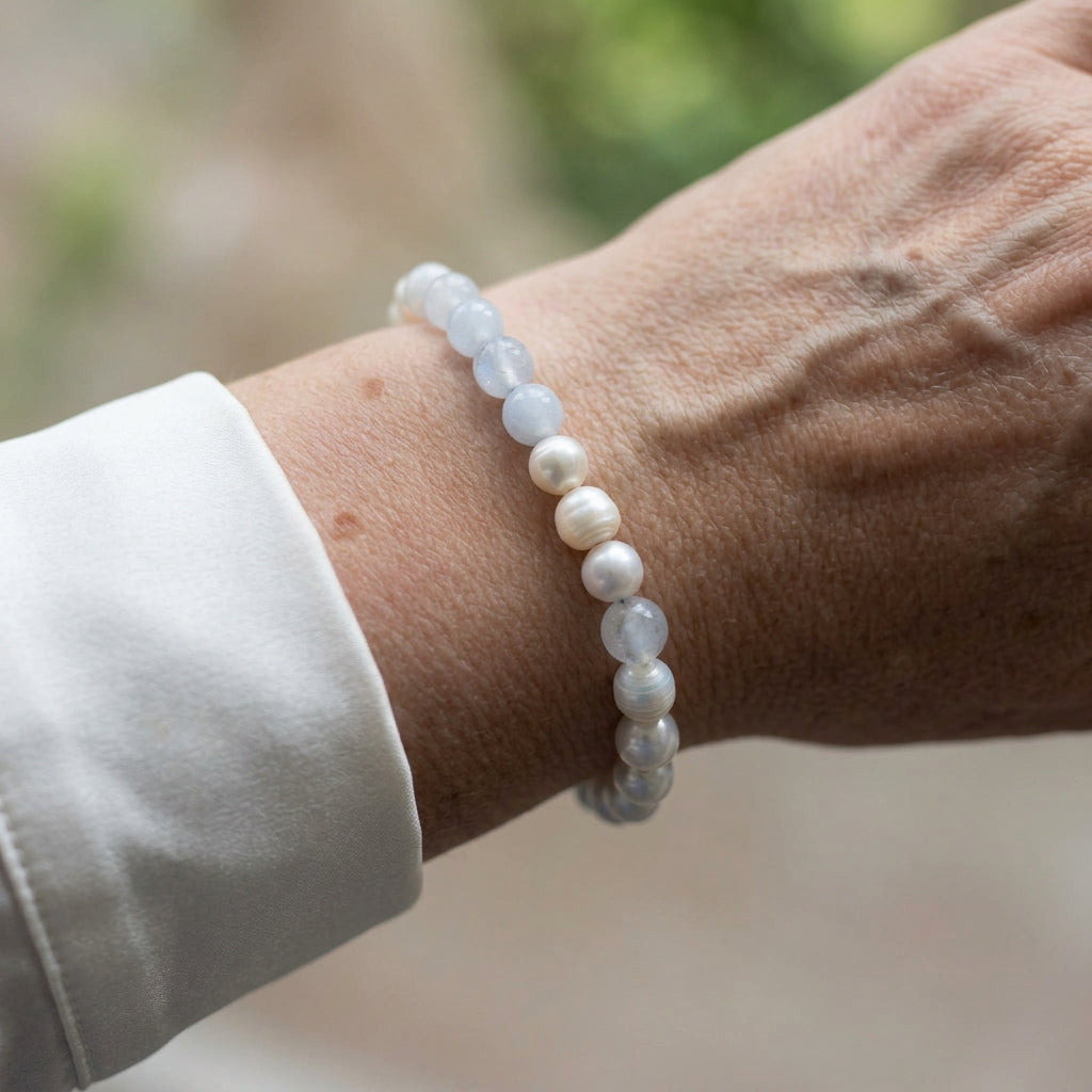 Pale blue aquamarine and white baroque pearl bracelet with three white pearls grouped at the centre, worn on the wrist beside a white silk shirt cuff.