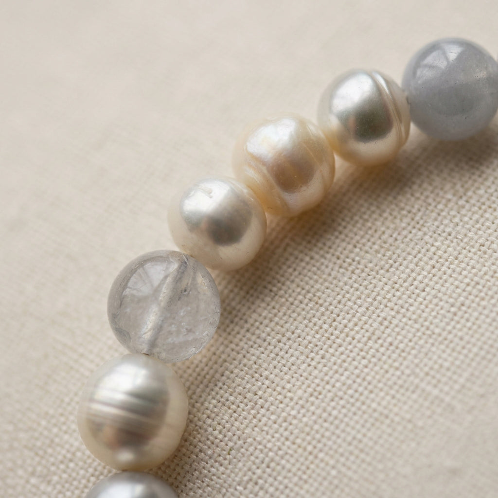 Close-up of white baroque pearls with natural ridges and soft lustre alongside translucent pale blue aquamarine beads on beige linen.