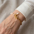 Pink quartz and white baroque pearl bracelet with a gold-coloured oval-link chain, fastened toggle clasp and dangling pearl charm, worn beside a white silk shirt cuff.