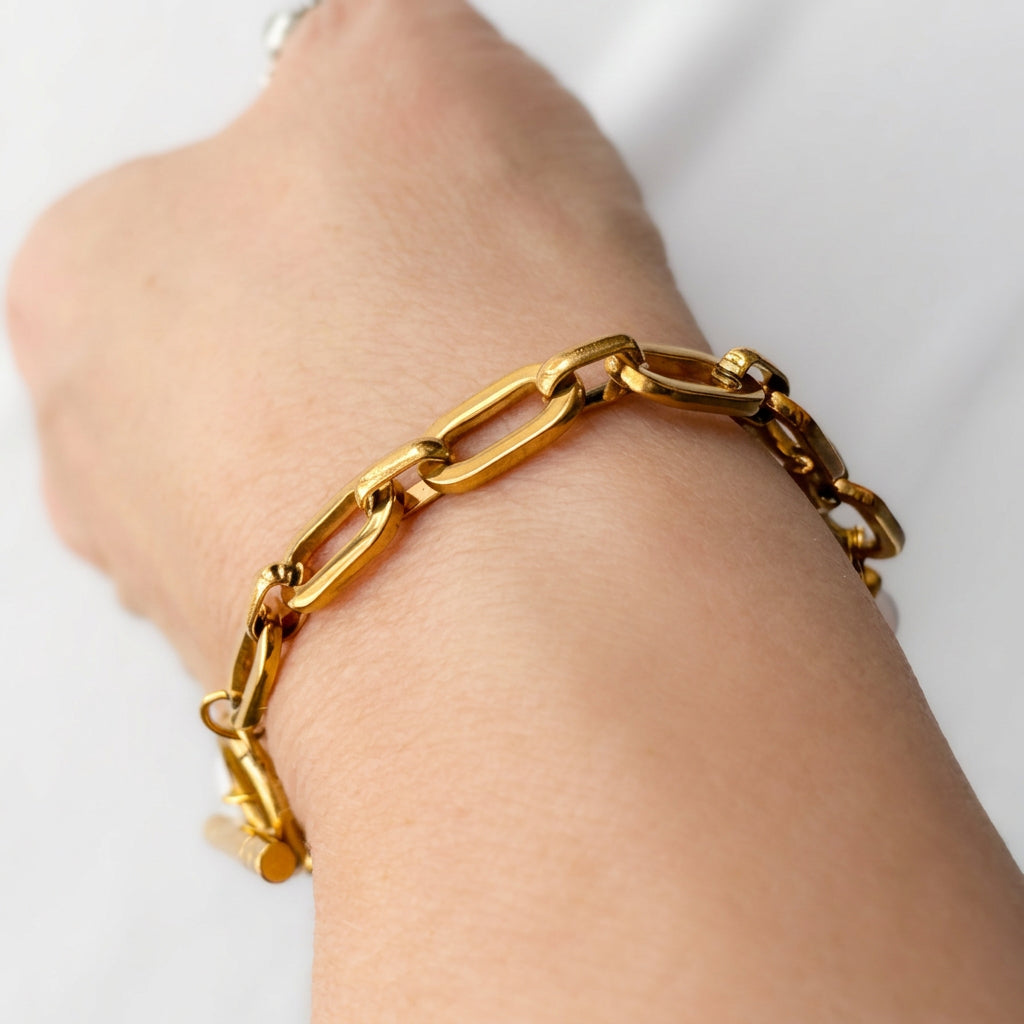 Close-up of the gold-plated paperclip chain side of a bracelet worn on a wrist, showing polished elongated rectangular links.