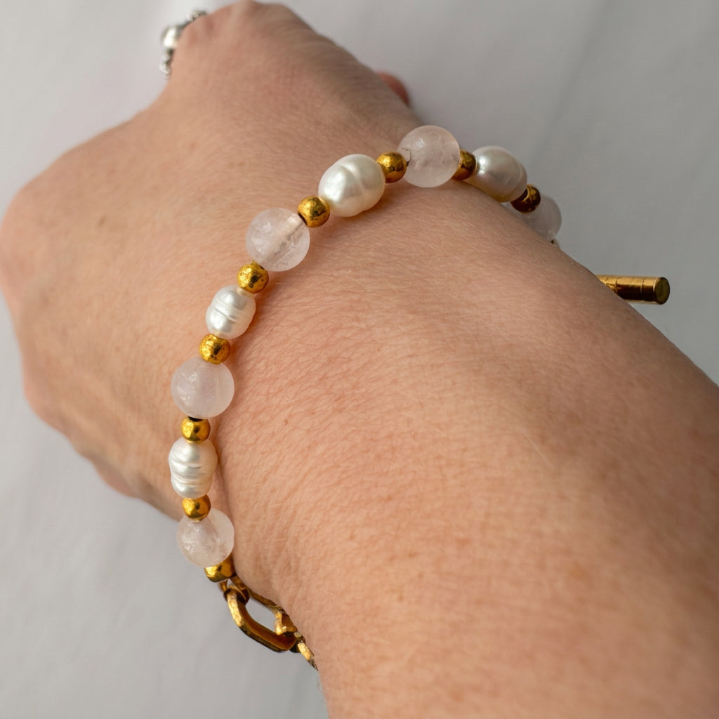 Close-up of the beaded side of a bracelet worn on a wrist, showing alternating pale pink quartz and white baroque pearls separated by small gold-coloured beads.