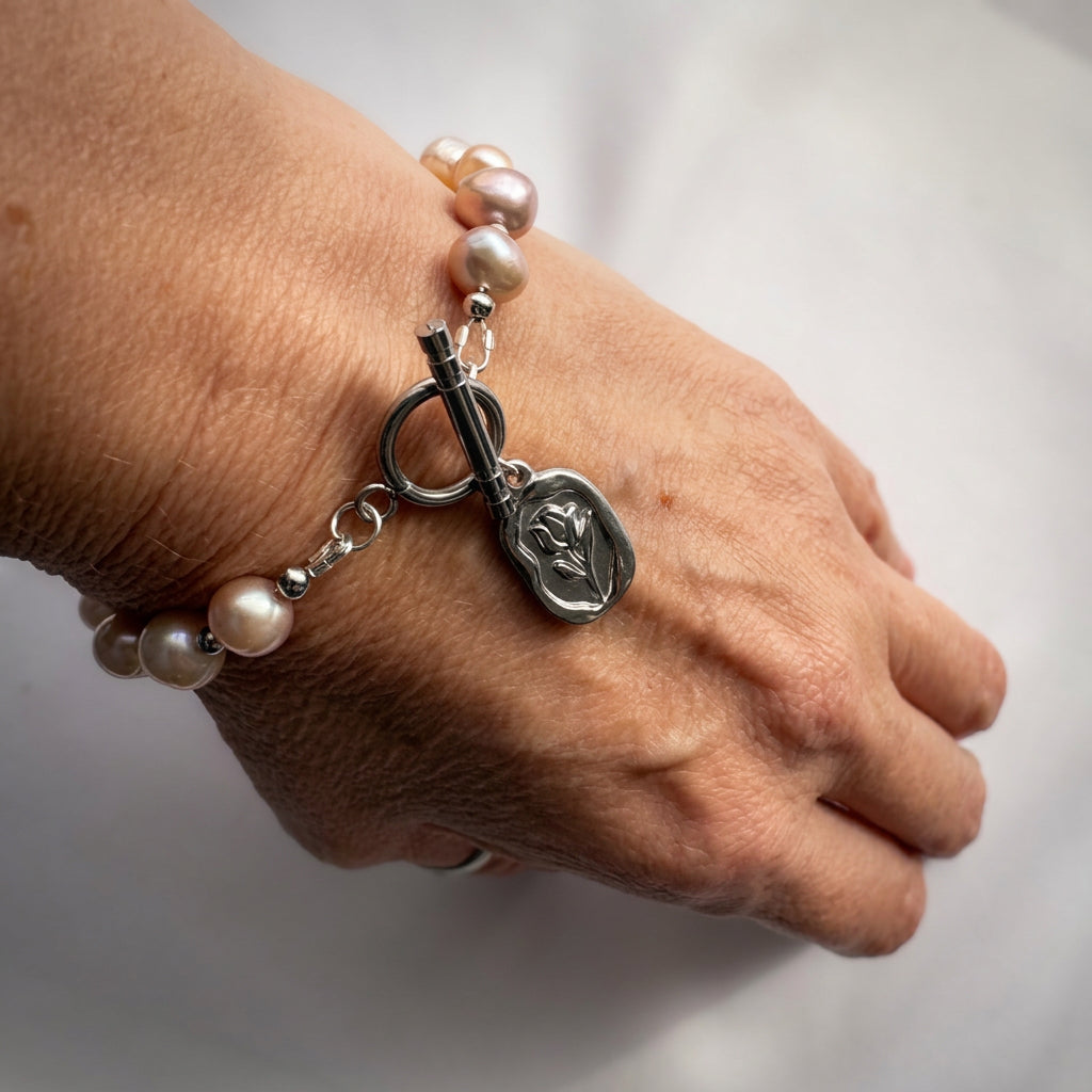 Angled view of a pink baroque pearl bracelet worn on a wrist, showing its stainless steel toggle clasp and dangling rectangular tulip pendant.